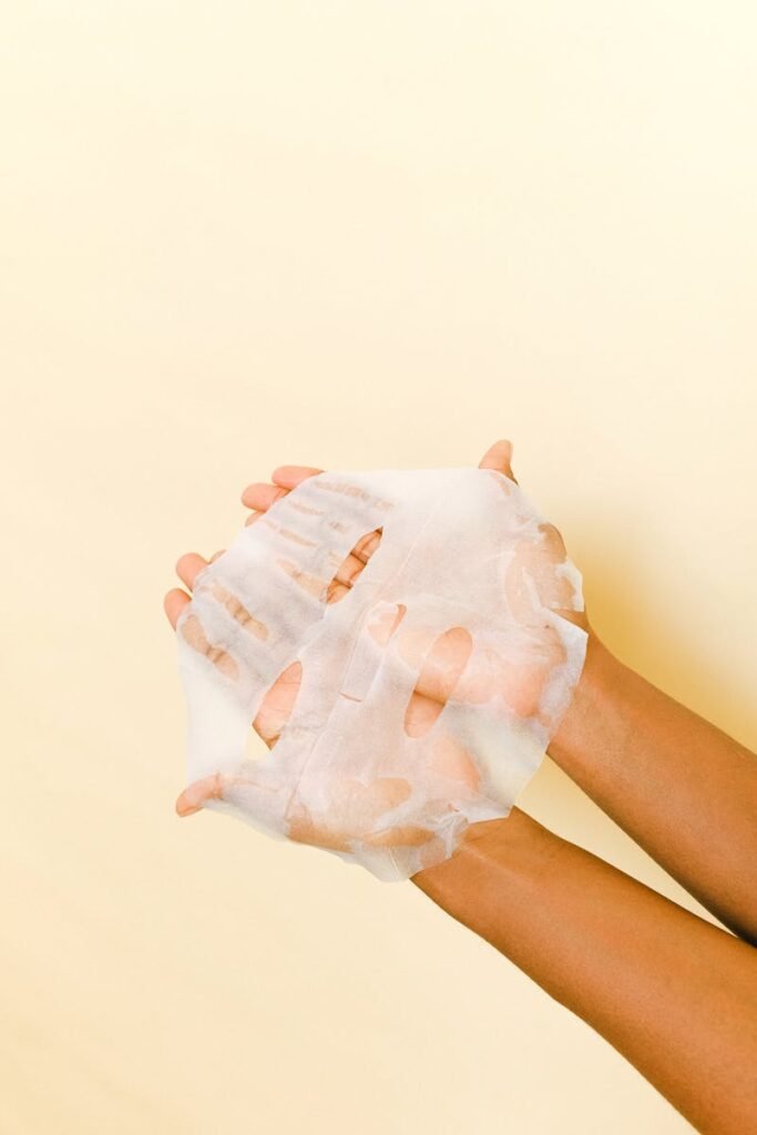 Martin Skincare Madrid - Close-up of hands holding a white sheet mask for skincare on a light background.