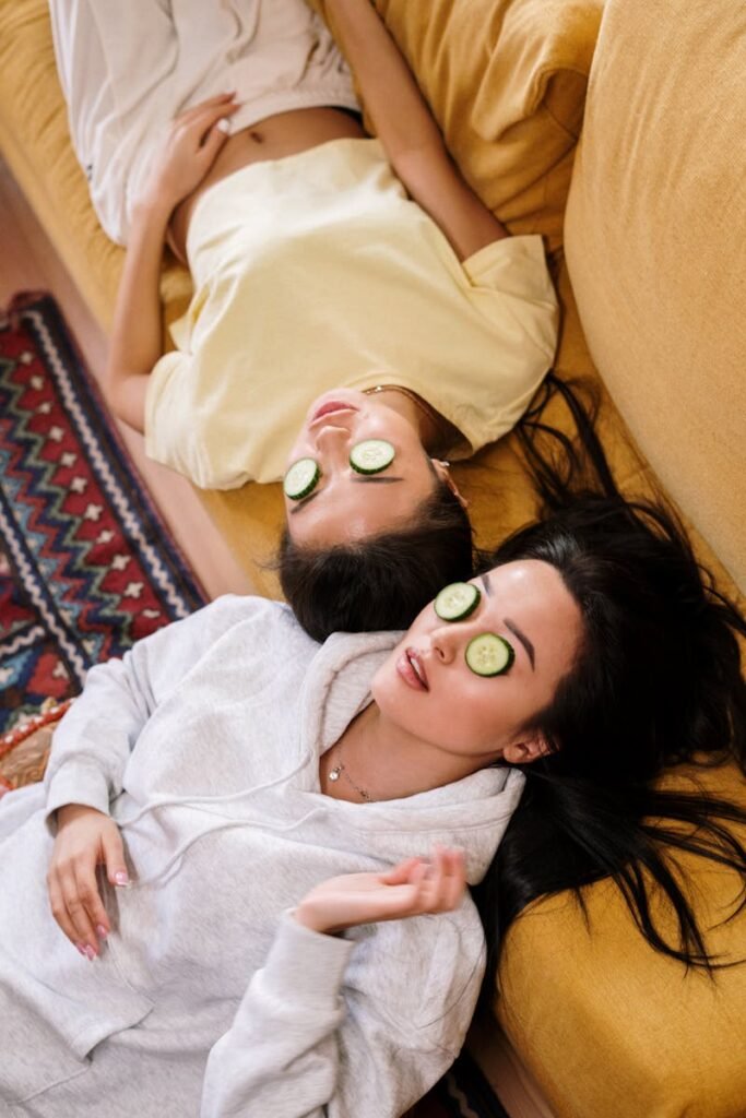 Two women enjoying a relaxing spa day with cucumber masks in a cozy home setting.